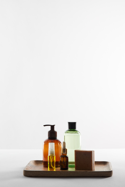 Vassoio in legno con vari contenitori cosmetici e sapone su superficie bianca
 - Foto, immagini
