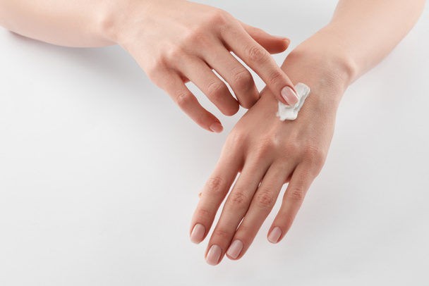Vista parcial de la mujer aplicando crema cosmética en las manos sobre fondo blanco
  - Foto, imagen