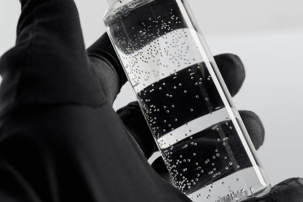 abgeschnittene Ansicht der weiblichen Hand in schwarzem Handschuh mit transparenter Kosmetikflasche auf weißem Hintergrund - Foto, Bild