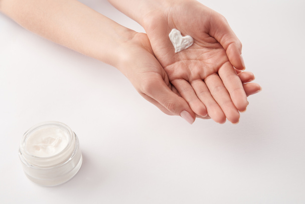 Partial view of woman applying cosmetic cream in heart shape on white background - Photo, Image
