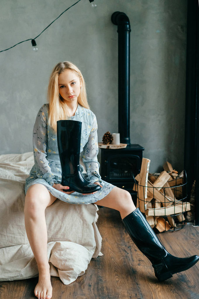Beautiful young blonde woman sitting on sofa while holding black boot - Foto, afbeelding