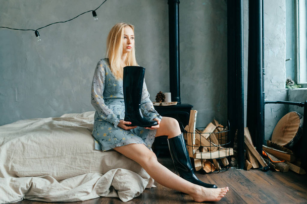 Beautiful young blonde woman sitting on sofa while holding black boot - Fotoğraf, Görsel