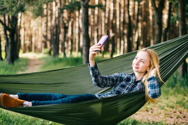 jonge vrouw nemen selfie op smartphone tijdens het rusten in de hangmat in bos - Foto, afbeelding