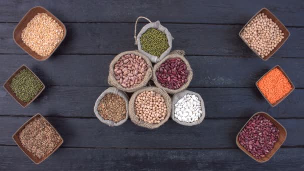Legumes on dark wooden ecological background.Beans are located in unusual form on black wooden table. Hands put bowls with beans on table. Bean cultures in wooden bowls. Healthy food in top view. - Footage, Video
