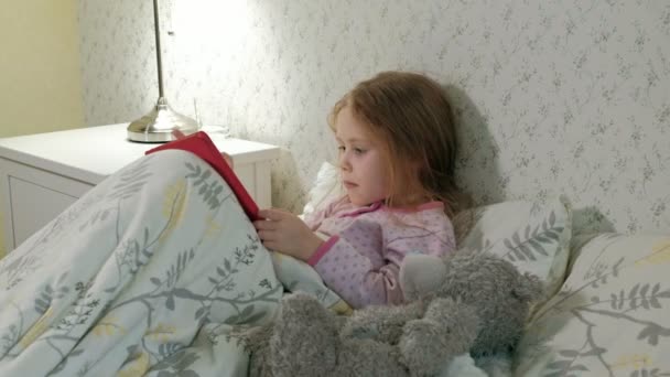 little girl in bed playing on tablet - Кадры, видео