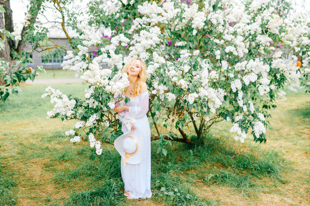 Young beautiful woman in white dress posing in spring blooming garden - Foto, Imagen