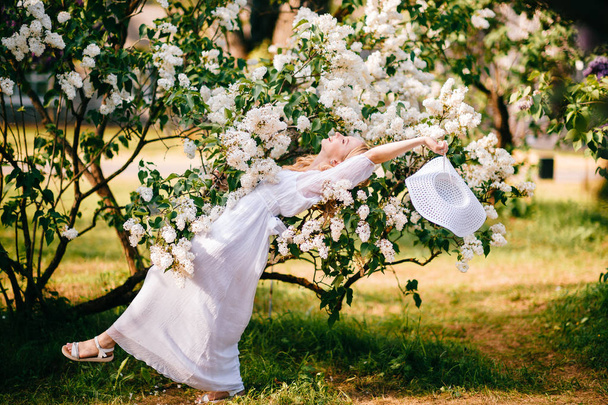 Young beautiful woman in white dress posing in spring blooming garden - Foto, afbeelding