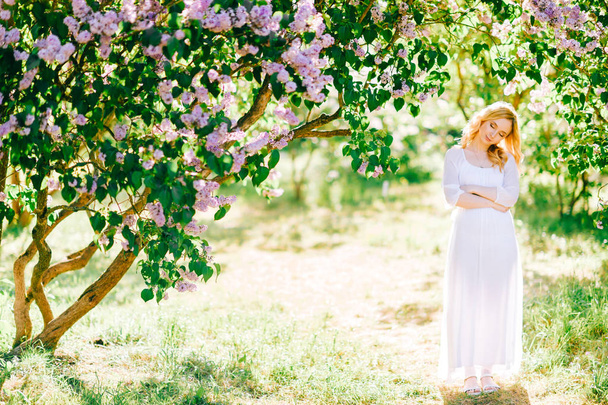 Young beautiful woman in white dress posing in blooming garden - Valokuva, kuva