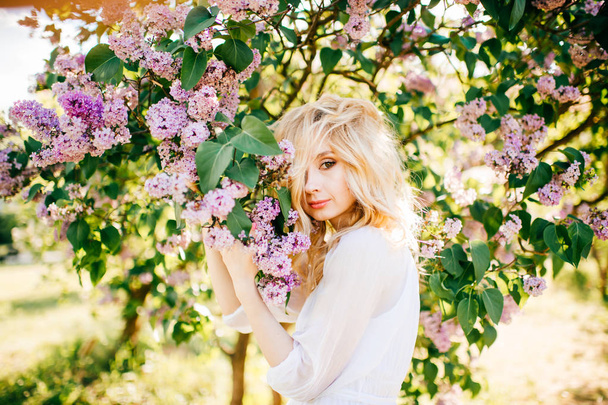 Young pretty blonde woman in white dress in blooming garden - Φωτογραφία, εικόνα
