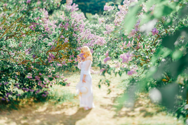Young pretty blonde woman in white dress in blooming garden - Foto, imagen