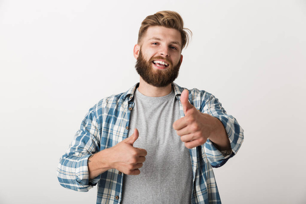 Image of a handsome young man standing isolated over white wall background showing thumbs up. - Zdjęcie, obraz