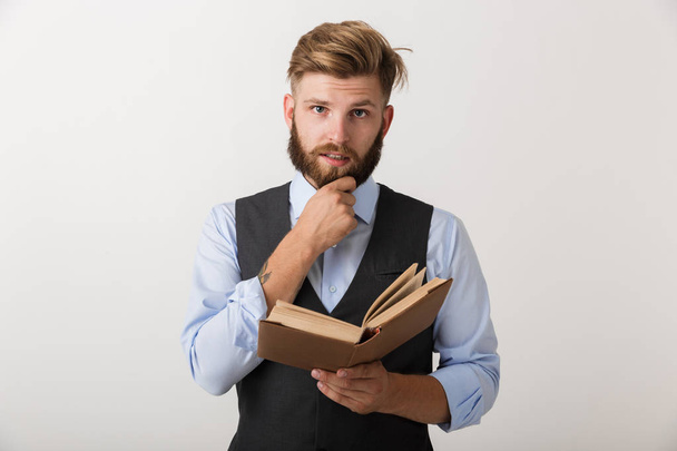 Image of a handsome young bearded man standing isolated over white wall background holding book reading. - Zdjęcie, obraz