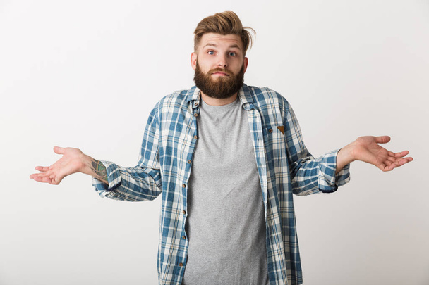 Confused young man dressed in plaid shirt standing isolated over white background - Foto, immagini