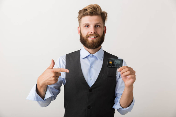 Luottavainen nuori liikemies seisoo eristyksissä valkoisella taustalla, näyttää luottokorttia
 - Valokuva, kuva