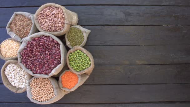 Legumes on dark wooden ecological background.Beans are located in the shape of circle on black wooden table. Bean cultures in knitted bags. Camera moves from right to left.  - Footage, Video