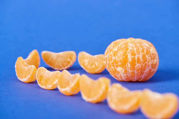 selective focus of tangerine slices near peeled clementine on blue background - Foto, Imagen