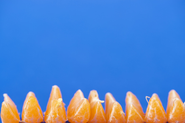 селективный фокус органических очищенных кусочков мандарина, выделенных на голубом
  - Фото, изображение