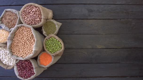Legumes on dark wooden ecological background.Beans are located in the shape of circle on black wooden table. Hands pour chickpeas in bag. Bean cultures in knitted bags. Camera moves from right to left.  - Footage, Video