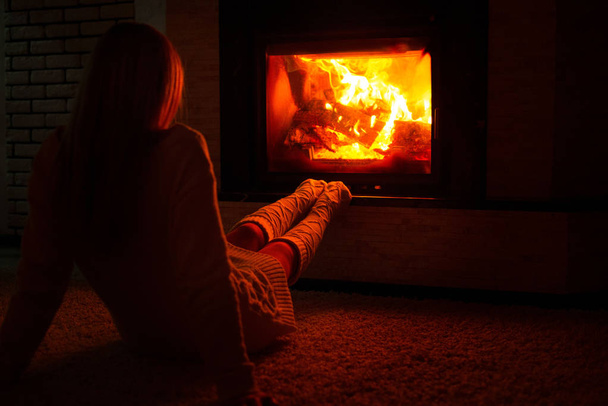 Une femme en chaussettes tricotées est assise près de la cheminée par une froide soirée d'hiver
. - Photo, image