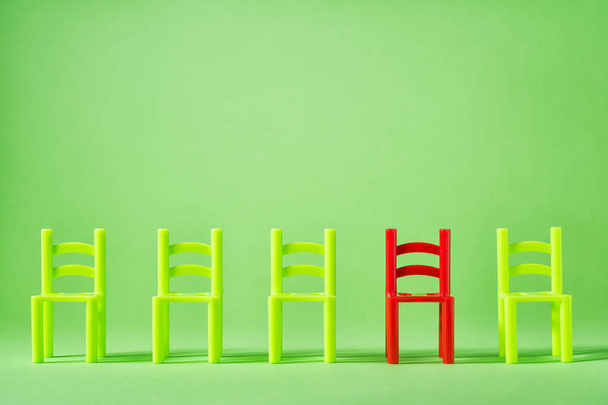 Μοναδική κόκκινη καρέκλα στην γραμμή της πράσινης άλλοι. Έννοια ηγεσία. Άδειες καρέκλες από τοίχο. Η έννοια της μοναδικότητας, διάκριση από άλλους. - Φωτογραφία, εικόνα