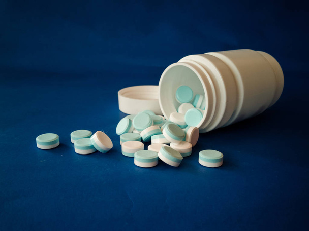 Drogas que fluem para fora do frasco em um fundo azul e o conceito de overdose
 - Foto, Imagem