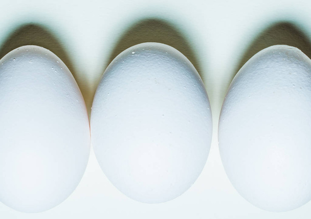 White chicken egg on a white background. Minimalistic background for easter cards. Pattern shades of light and shadow - Foto, afbeelding