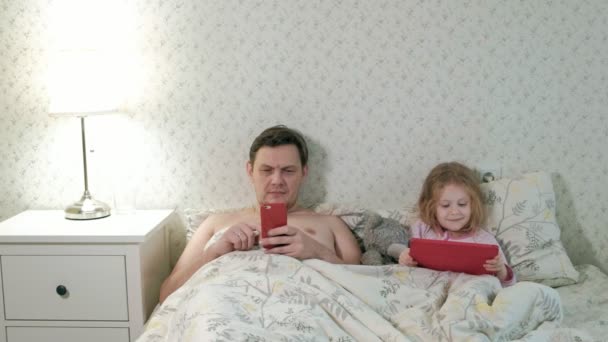 isä ja pieni tytär sängyllä leikkii tabletilla
 - Materiaali, video