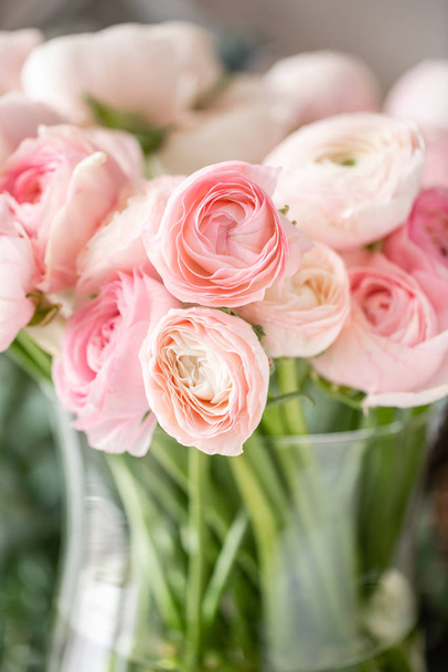 Περσικό βούτυρο σε γυάλινα βάζα. Ένα μάτσο χλωμά ροζ λουλούδια του ranunculus φωτίζουν το φόντο. Ταπετσαρία. Άνθη χειμερινής περιόδου - Φωτογραφία, εικόνα