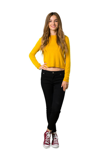A full-length shot of a young girl with yellow sweater posing with arms at hip and smiling on isolated white background - Fotoğraf, Görsel