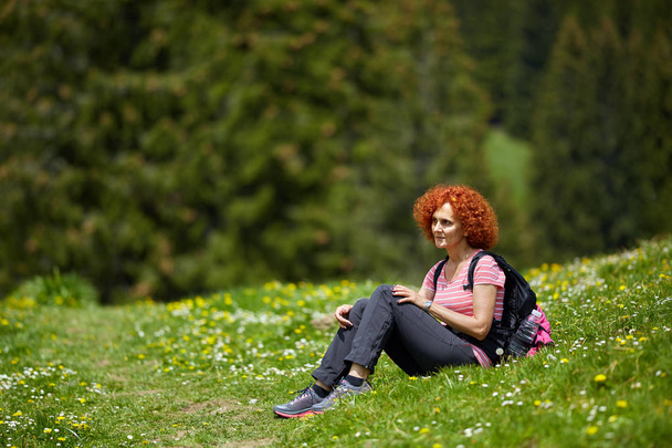 Curly redhead woman with backpack hiking on trail at daytime - Foto, Imagem