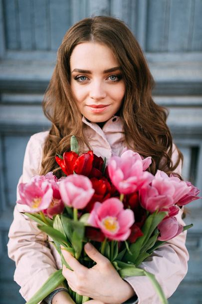 beautiful young woman with bouquet of tulips posing on street - Fotó, kép