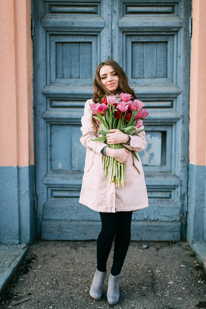 beautiful young woman with bouquet of tulips posing on street - Foto, Imagen