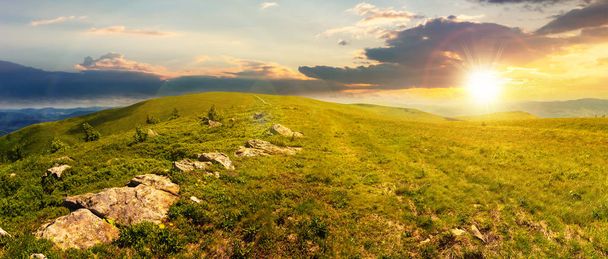 Panorama van prachtige Karpaten alpenweiden bij zonsondergang in avondlicht. prachtige zomer landschap. pluizige wolken op de blauwe hemel. stenen aan de rand van een heuvel - Foto, afbeelding