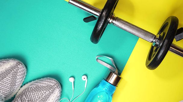 Top view layout with fitness equipment and space for text on yellow blue color background. healthy and active lifestyles love concept sports sneakers, dumbbell, bottle of waters, apple, headphones. - Fotografie, Obrázek