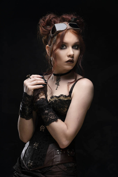 A beautiful redhead cosplayer girl wearing a Victorian-style steampunk costume with big breasts in a deep neckline looks surprised and scared. Portrait. Black background. Copy space. - Fotoğraf, Görsel