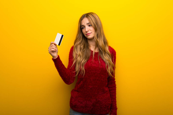 Νεαρό κορίτσι με ζωντανό κίτρινο φόντο, λαμβάνοντας μια πιστωτική κάρτα χωρίς χρήματα - Φωτογραφία, εικόνα