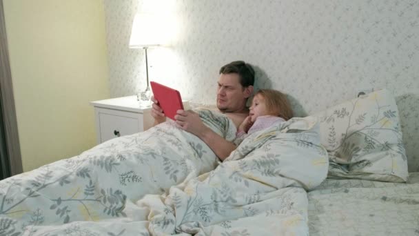 dad and little daughter on the bed playing on the tablet - Metraje, vídeo