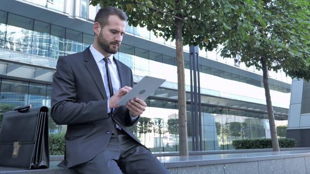Uomo d'affari che utilizza il computer tablet mentre seduto fuori dall'ufficio
 - Foto, immagini