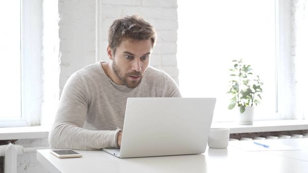Homem barba em choque enquanto trabalhava no laptop, surpreendido
 - Foto, Imagem