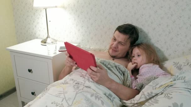 ο μπαμπάς και η μικρή της κόρη για το κρεβάτι έπαιζαν στο tablet - Πλάνα, βίντεο