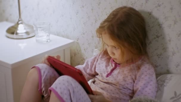 little girl in bed playing on tablet - Záběry, video