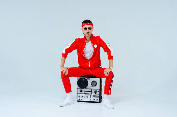 cheerful fashionable man wearing a red sports suit sitting with a retro tape recorder. proud and successful style of the 90's. - Foto, immagini
