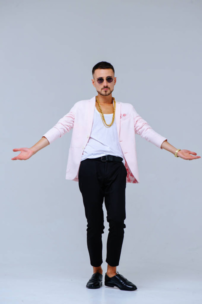 fashionable sophisticated man in a pink jacket and black trousers, wears a gold chain, the expression of emotions gestures with his hands. - Φωτογραφία, εικόνα