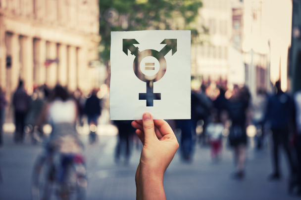 Bir kağıt sayfası transseksüel sembolü ve eşittir işareti içinde tutan el. Cinsiyet kavram bir kalabalık şehir sokak arka plan üzerinde arasında eşitlik. Seks hakları sosyal sorunun bir metafor olarak. - Fotoğraf, Görsel