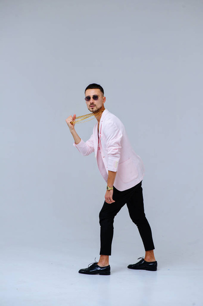 divatos kifinomult ember egy rózsaszín zakó és fekete nadrág, egy arany láncot hord, az érzelmek kifejezése gesztusok a kezével. - Fotó, kép