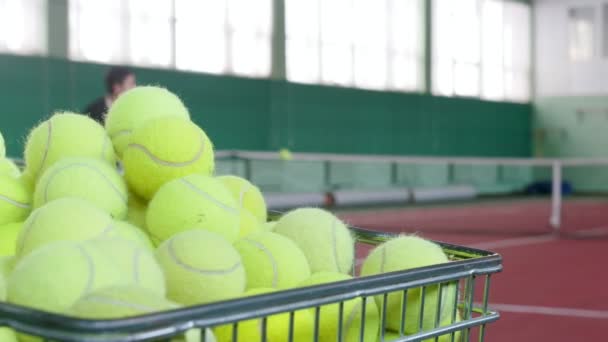 2 つの若い男性のテニスコートでテニスをプレーします。トレーニング。前景にテニス ・ ボールでいっぱいカート - 映像、動画