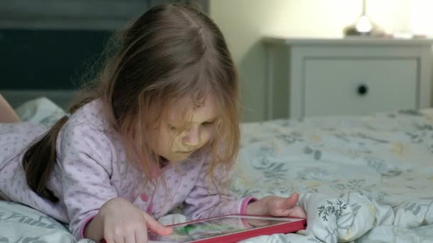 little girl in bed playing on tablet - Кадры, видео