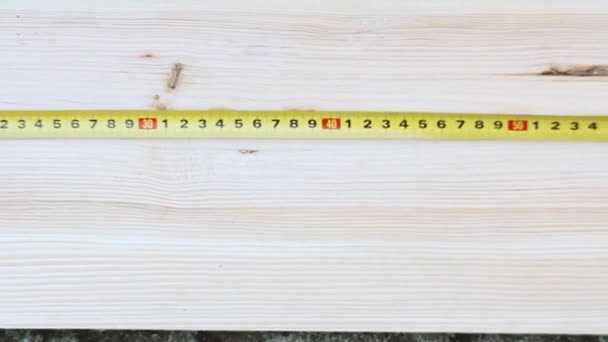 Lähikuva puuseppä mittaa puinen työpöytä keltaisella teipillä toimenpide työpajassa. Mies valkoisissa hanskoissa.
 - Materiaali, video