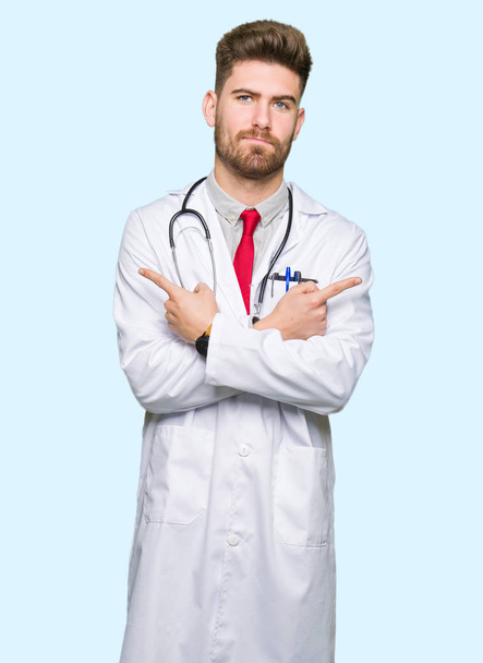 Young handsome doctor man wearing medical coat Pointing to both sides with fingers, different direction disagree - Foto, Bild