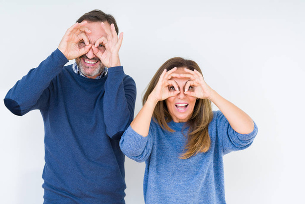 Beautiful middle age couple in love over isolated background doing ok gesture like binoculars sticking tongue out, eyes looking through fingers. Crazy expression. - Foto, immagini